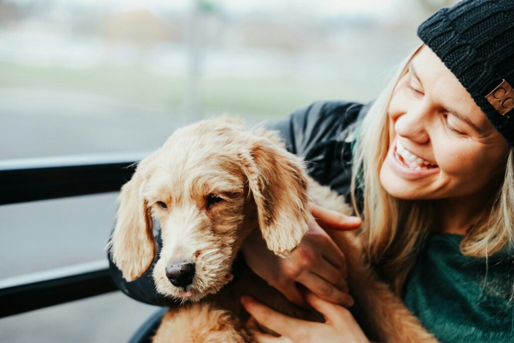 smiling woman wearing gray jacket carrying beige Labradoodle
